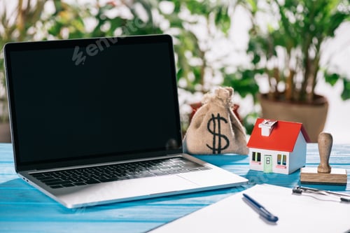 Preview: selective focus of pen, clipboard, laptop with blank screen near stamp, house model and moneybag