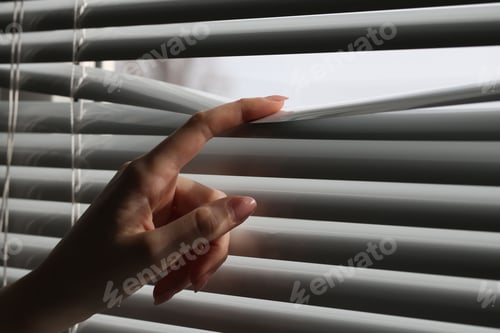 Preview: Woman separating slats of white blinds indoors, closeup