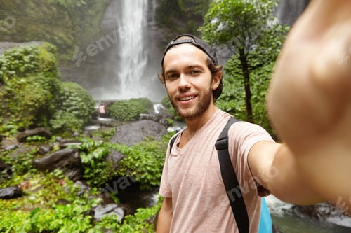 Preview: People, lifestyle, nature and adventure concept. Stylish young traveler with knapsack holding camera
