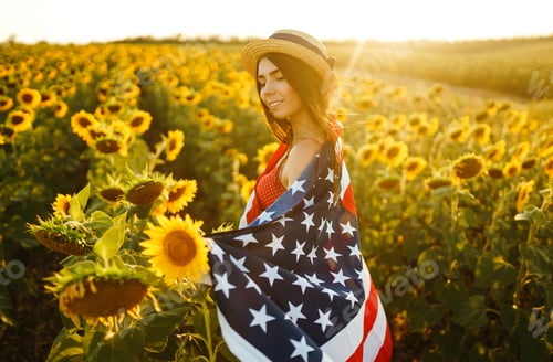 Preview: Beautiful girl in hat with American flag in sunflower field. 4th of July. Independence Day.