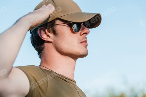 Preview: side view of young soldier in cap and sunglasses against blue sky