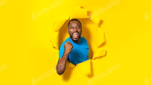 Preview: Overjoyed african american man raising clenched fist and shouting, breaking through yellow paper