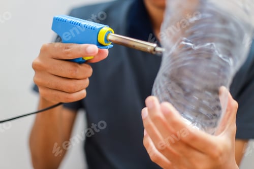 Preview: Close Up Of Person's Hands Using Soldering Iron To Create Holes In Clear Plastic Bottle