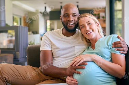 Preview: Loving Multi-Racial Couple With Pregnant Woman On Sofa At Home With Multi-Generation Family Behind