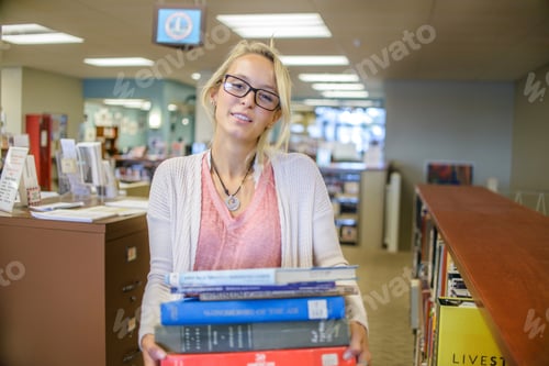 Preview: Portrait of young female librarian carrying stack of books
