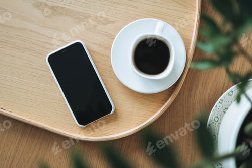 Preview: Top view of smartphone screen and cup of coffee through green houseplant
