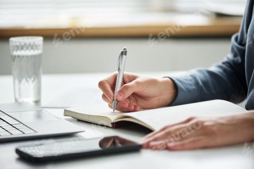 Preview: Hand of young businesswoman holding pen over page of open notepad