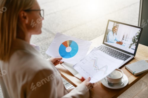 Preview: Businesswoman making online videoconference and demonstrate financial graphs to colleague in cafe