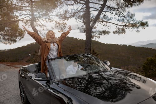 Preview: Cheerful Caucasian beautiful woman raised her hands in the air standing in convertible car