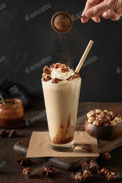Preview: Tasty banana milkshake garnish caramel and whipped cream sprinkled cacao powder on dark. Close up.