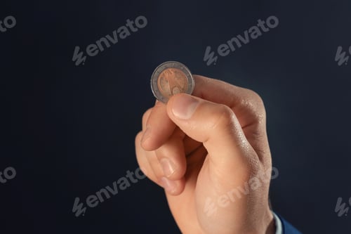 Preview: Young man holding coin on dark background, closeup