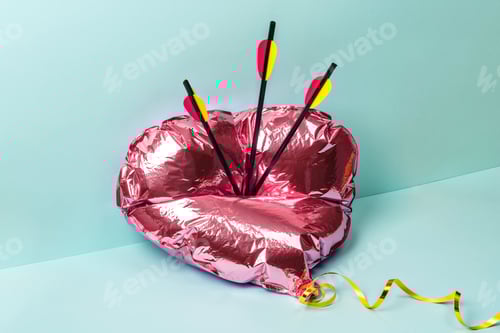 Preview: Foil pink heart balloon punctured by three arrows on a pastel surface