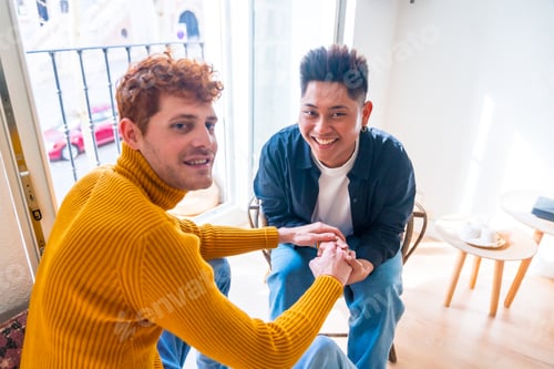 Preview: Portrait of beautiful gay couple being romantic at home by the balcony holding hands, lgbt concept