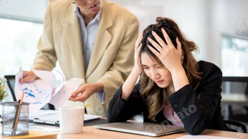 Vista previa: Asian businesswoman holding head in pain or getting stressed after making mistake at office's table.