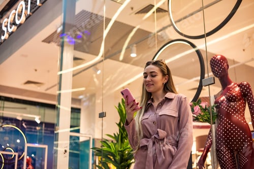Preview: Lovely smiling lady using mobile phone at window store shop center, enjoying looking