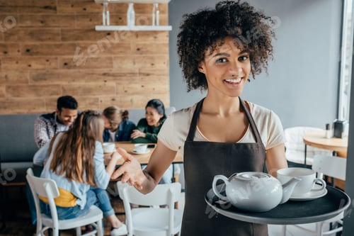 Preview: Smiling african american waitress holding tray with tea and customers sitting behind her in cafe