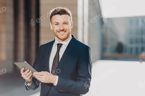 Preview: Portrait of handsome male with positive expression, updates software on tablet computer