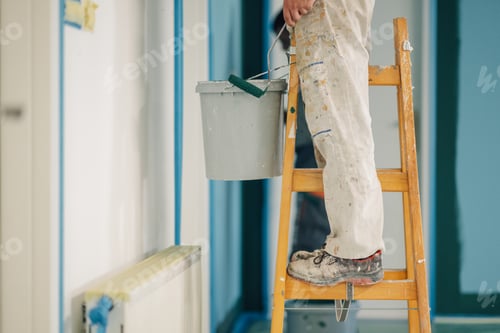 Preview: Painter working on wooden ladder holding paint bucket during home renovation