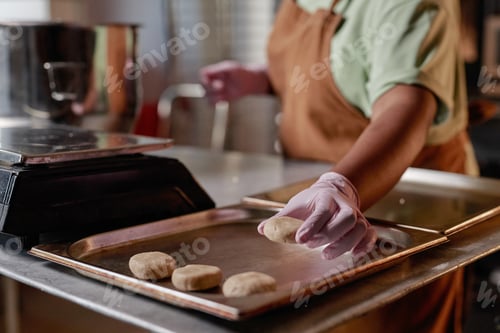 Preview: Black Woman Working in Gloves Putting Rounded Dough on Tray Making Cookies in Bakery