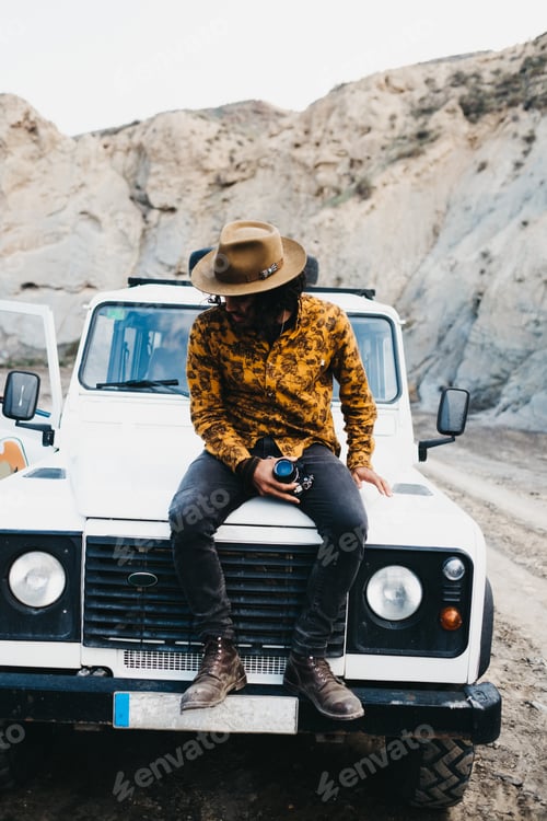 Preview: Stylish man sitting on car in canyon