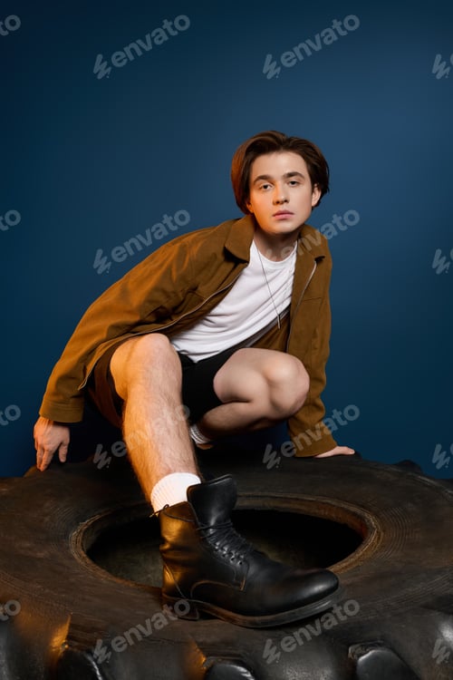 Preview: Young fashionable man poses creatively on unique backdrop showcasing style and confidence