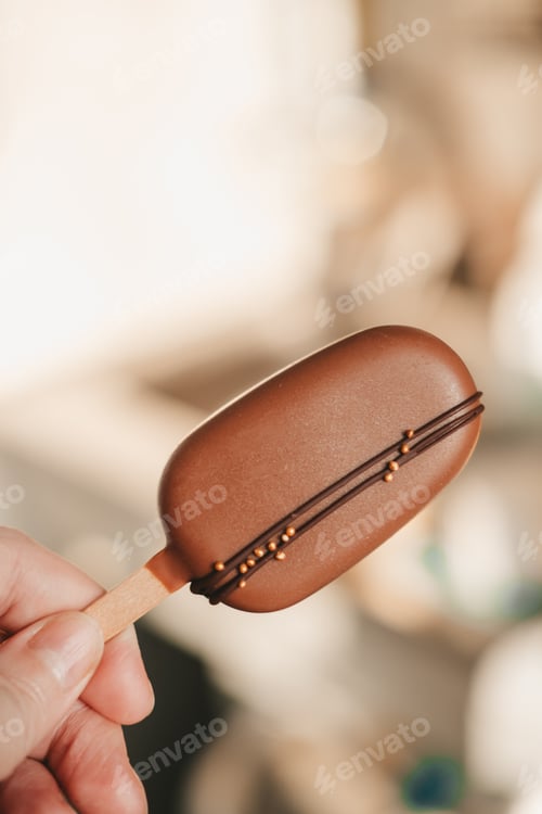 Preview: chocolate cake on a stick in hands close-up. delicious chocolate cake ice cream for coffee.
