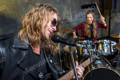 Preview: Handsome man playing electric guitar and woman sitting at drums set in musical studio
