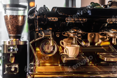 Preview: coffee pouring from coffee machine in cup near blurred grinder with sunlight in cafe