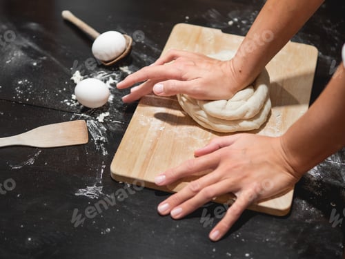 Preview: Woman kneads dough with flour and eggs on black wooden table. Cooking at home.