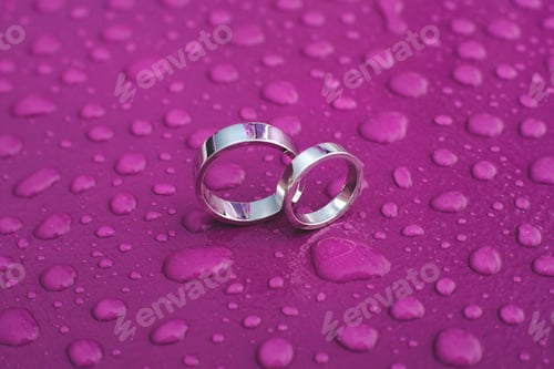Preview: Wedding rings on a pink surface in the rain.