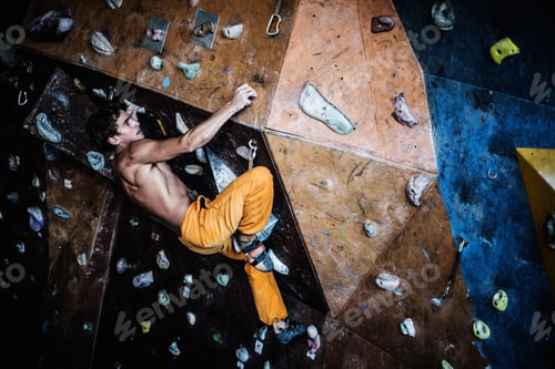 Preview: Muscular man practicing rock-climbing on a rock wall indoors