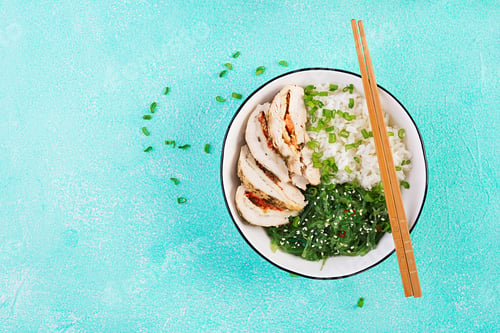 Preview: Healthy salad in a white bowl, chopsticks. Chicken rolls, rice, chuka and green onion.