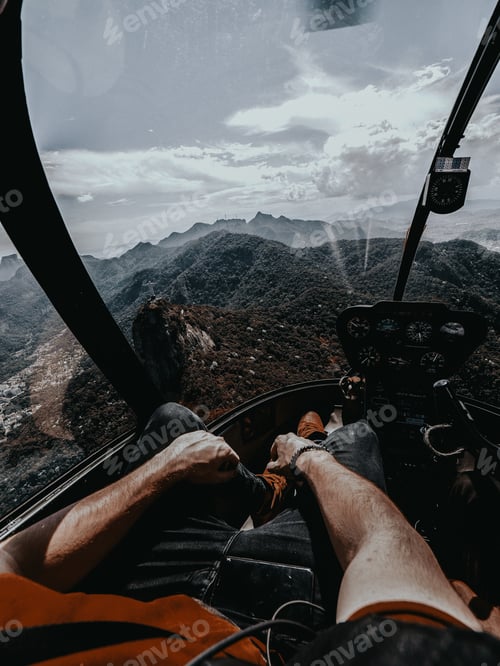 Preview: Vertical shot of a person sitting in a helicopter flying over the mountains