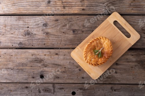 Preview: Overhead view of baked stuffed pie with rosemary on wooden serving board at table
