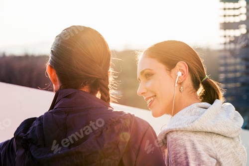 Preview: Two female friends outdoors, smiling, rear view