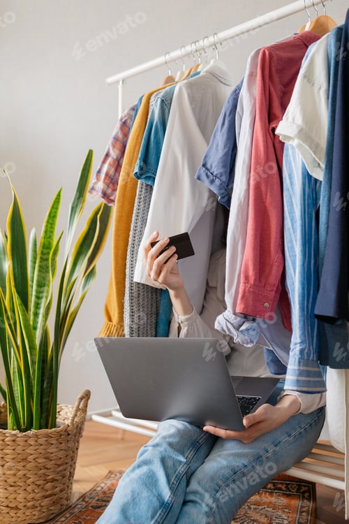 Preview: caucasian woman among the clothes in her closet with a laptop and a credit bank card