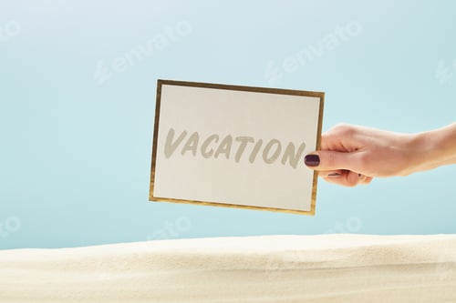 Preview: cropped view of woman holding card with vacation lettering in hand isolated on blue