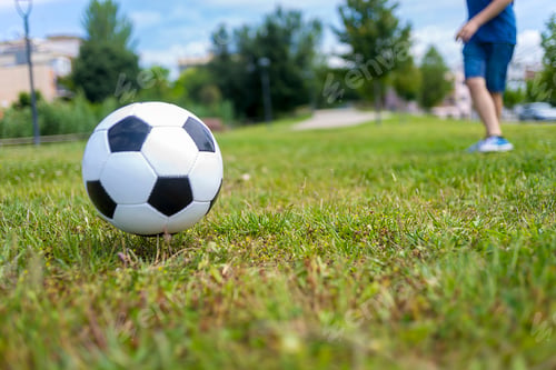 Preview: Low angle view of a ball on park grass kicked by a child