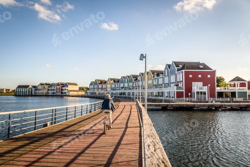 Preview: Cyclist crossing a bridge near colorful row houses at dusk and reflections on water in Houten