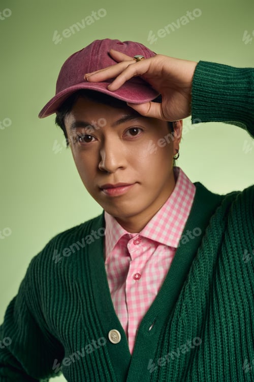 Preview: Stylish asian man showcases fashion flair in vibrant green studio setting