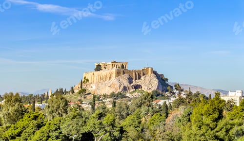 Preview: Ancient Acropolis hill above Athens upon bright day, viewed over green trees under clear blue sky