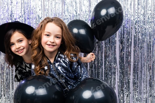 Preview: black Friday. two cute stylish young sisters in holiday dresses with black balloons at a party on a