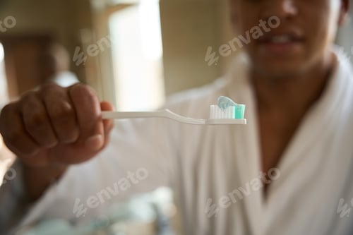 Preview: Focus of toothbrush in hand of blurred african american man in bathroom