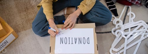 Preview: A beautiful Asian woman uses a magic marker to write on a box of clothes that will be donated to