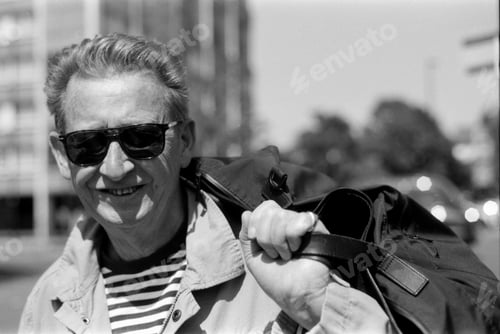 Preview: Smiling senior man carrying bag on shoulder in city
