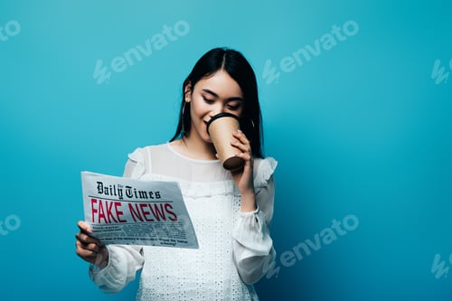 Preview: asian woman in white blouse holding newspaper with fake news and drinking coffee on blue background