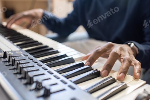 Preview: Fingers of young African man pressing keys of music keyboard
