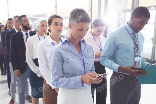 Preview: Diverse business people standing in queue in lobby at office and looking their mobile phone