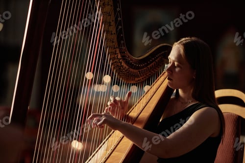 Preview: Young Woman Strumming Harp Strings Playing Classical Music in Dim Light Indoors