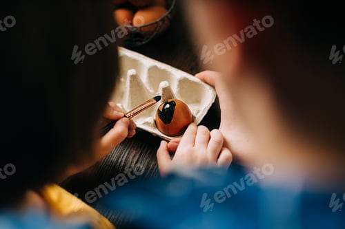 Preview: Easter day. Male Father and son painting eggs on wooden background. Family sitting in a kitchen